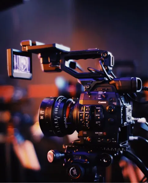 A professional Canon cinema camera rig equipped with a cine lens and external monitor, set against a blurred background.
