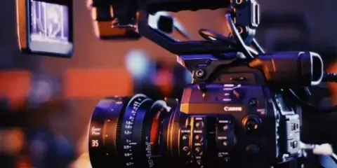 A professional Canon cinema camera rig equipped with a cine lens and external monitor, set against a blurred background.
