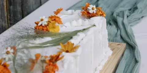 A white frosted wedding cake decorated with orange and white flowers on a wooden board.