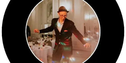 A man in a suit and hat performing as a DJ at a wedding reception.