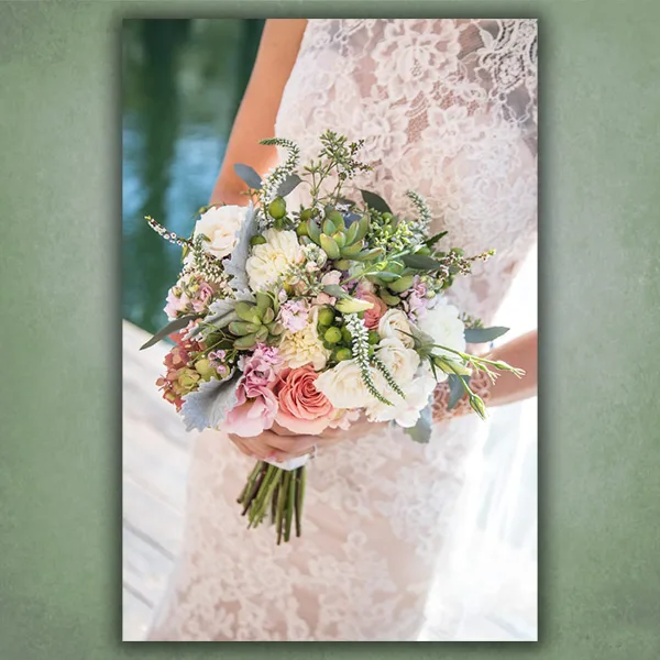 A bride in a lace dress holding a mixed bouquet of white and pink flowers with greenery.