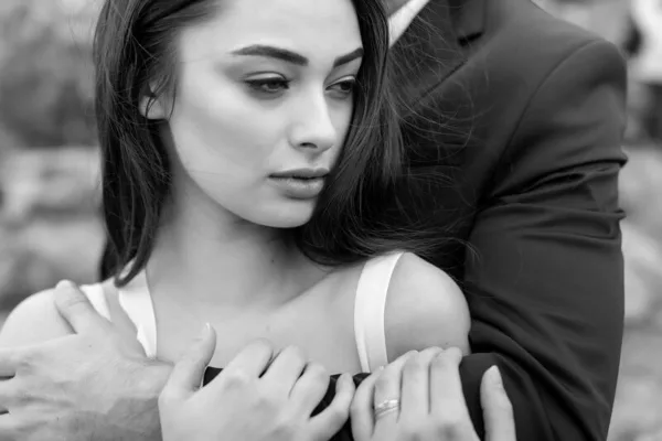 Black-and-white close-up of a bride's face showing styled hair and bridal makeup, leaning against a groom in a suit.