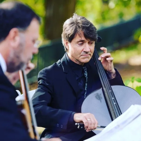 Two musicians in formal black attire performing strings outdoors at a wedding.