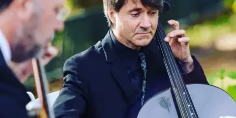 Two musicians in formal black attire performing strings outdoors at a wedding.