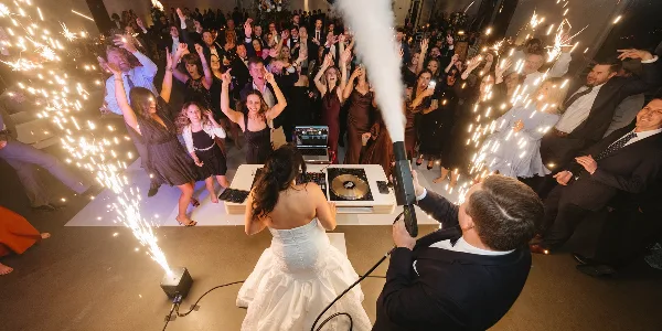A DJ performing at a wedding reception with a bride, groom, and guests celebrating with sparklers.