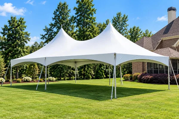 A large white high-peak frame tent set up on a green lawn in front of a house.