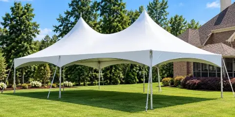 A large white high-peak frame tent set up on a green lawn in front of a house.
