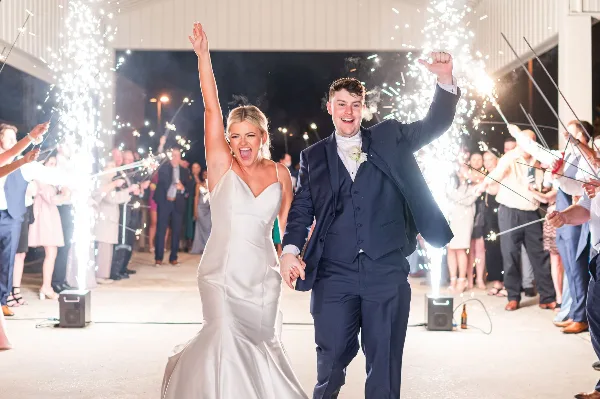 A bride and groom walking through a sparkler tunnel at a wedding reception with professional audio equipment visible.