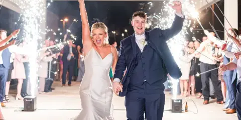 A bride and groom walking through a sparkler tunnel at a wedding reception with professional audio equipment visible.