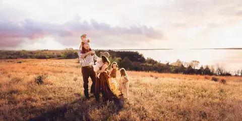 A family of six posing in a golden grassy field near a body of water during sunset.