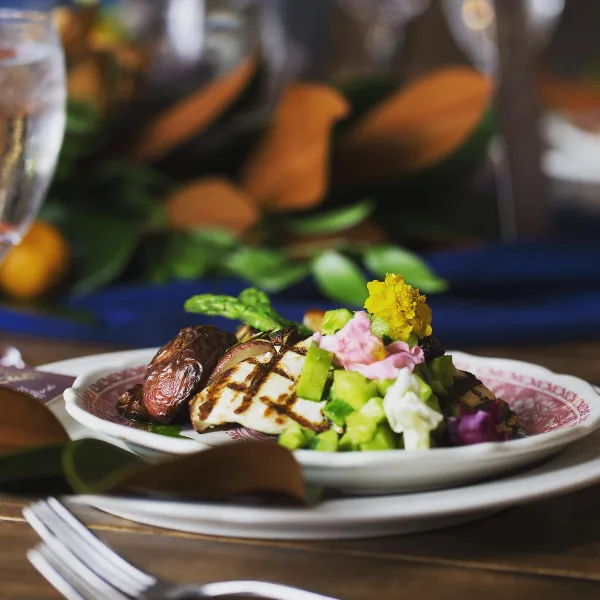A plated catering dish featuring grilled protein, asparagus, and edible flowers on a patterned plate.