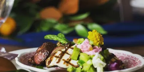 A plated catering dish featuring grilled protein, asparagus, and edible flowers on a patterned plate.