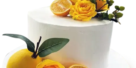 A white frosted cake decorated with yellow roses, green leaves, and fresh citrus fruit.