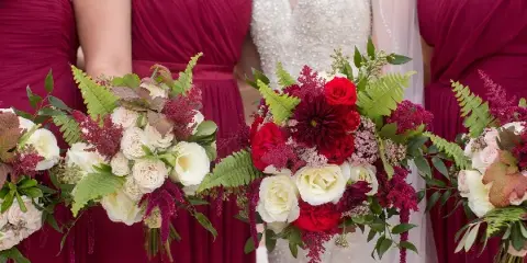 A bride in a white beaded dress and bridesmaids in maroon dresses holding floral bouquets.
