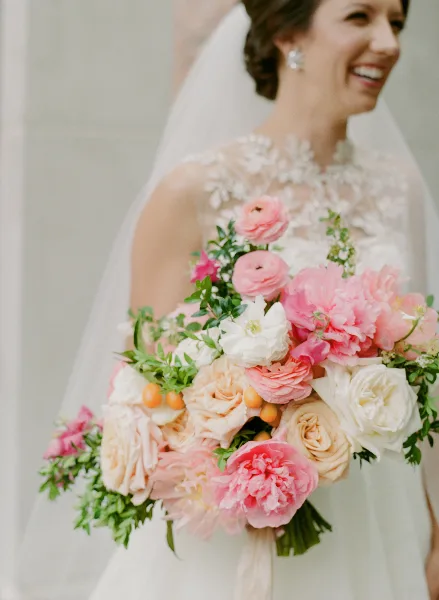 A bride in a white lace dress holding a large bouquet of pink and white flowers.