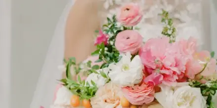 A bride in a white lace dress holding a large bouquet of pink and white flowers.