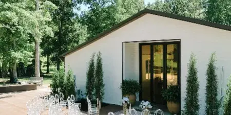 Outdoor wedding ceremony setup with rows of clear chairs on a wooden deck in front of a white Pavilion building.