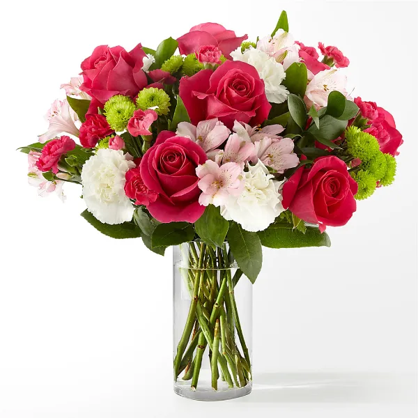 A vibrant floral arrangement containing pink roses, white carnations, and green button chrysanthemums in a clear glass vase.