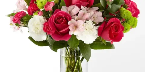 A vibrant floral arrangement containing pink roses, white carnations, and green button chrysanthemums in a clear glass vase.