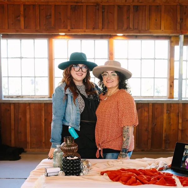 Two women standing behind a table with beauty supplies in a studio setting.