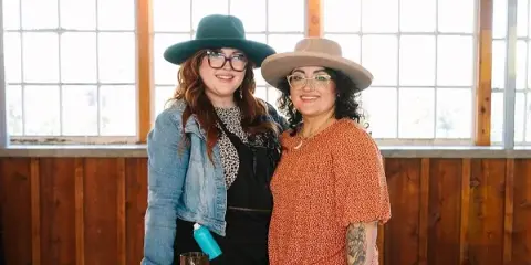 Two women standing behind a table with beauty supplies in a studio setting.