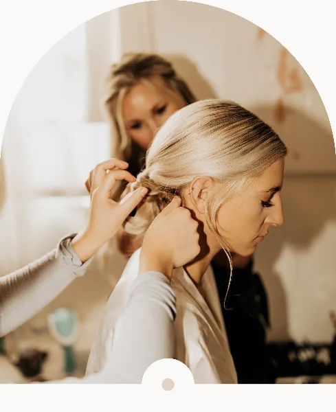 A professional stylist styling a bride's hair into an updo.