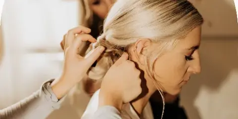 A professional stylist styling a bride's hair into an updo.