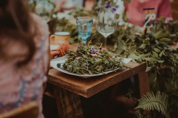 A close-up of a fresh green salad served on a white plate at a wooden table setting.