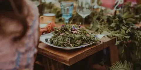 A close-up of a fresh green salad served on a white plate at a wooden table setting.