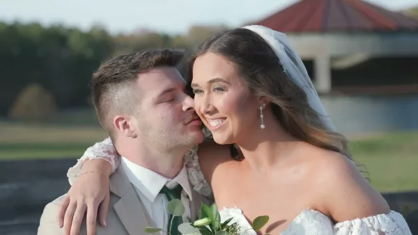A professional wedding photograph showing a groom kissing the cheek of a smiling bride.