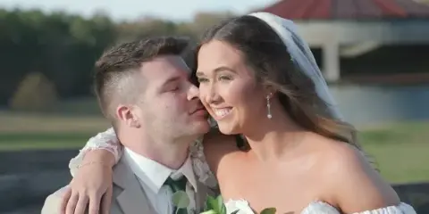 A professional wedding photograph showing a groom kissing the cheek of a smiling bride.