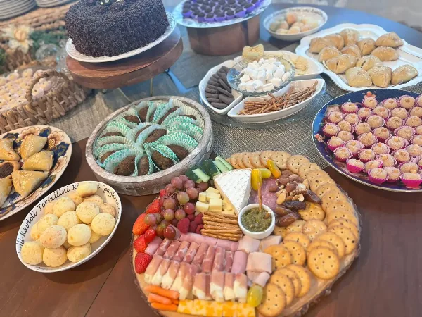 A professionally arranged catering table featuring a large charcuterie board with meats and cheeses, a bowl of chocolate truffles, and various pastries.
