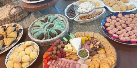 A professionally arranged catering table featuring a large charcuterie board with meats and cheeses, a bowl of chocolate truffles, and various pastries.