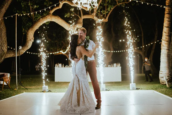 Couple dancing at an outdoor wedding reception at night with string lights and sparkler effects.