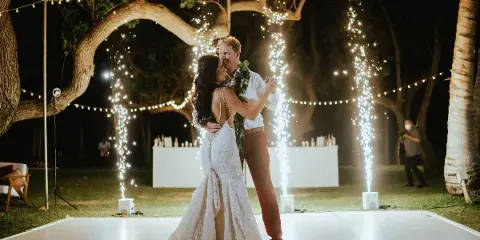 Couple dancing at an outdoor wedding reception at night with string lights and sparkler effects.
