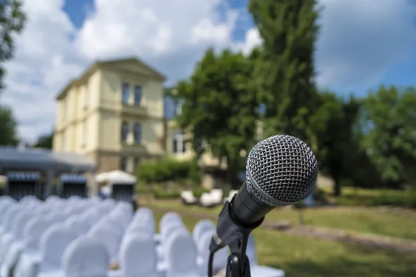 A close-up of a microphone on a stand with a wedding venue and rows of chairs in the background.