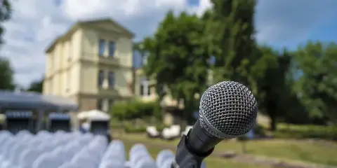 A close-up of a microphone on a stand with a wedding venue and rows of chairs in the background.