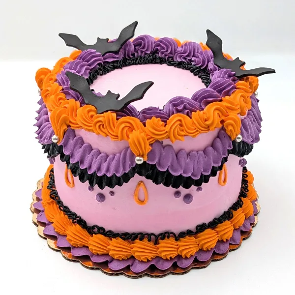 A two-tiered cake decorated with purple, orange, and black frosting, featuring fondant bat toppers.