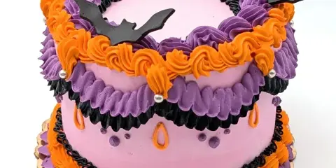 A two-tiered cake decorated with purple, orange, and black frosting, featuring fondant bat toppers.