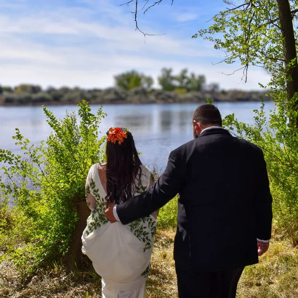 A bride and groom standing together in a natural outdoor setting near a body of water.