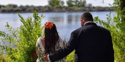 A bride and groom standing together in a natural outdoor setting near a body of water.