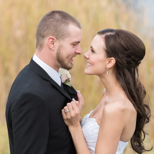 A bride and groom smiling at each other in a field during a wedding session.