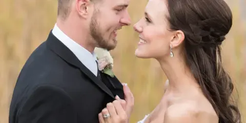 A bride and groom smiling at each other in a field during a wedding session.