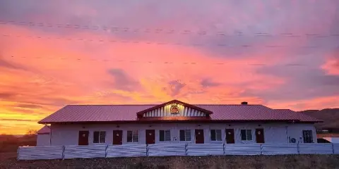 Single-story white ranch building with a red roof and multiple doors, set against a vibrant pink and orange sunset sky.