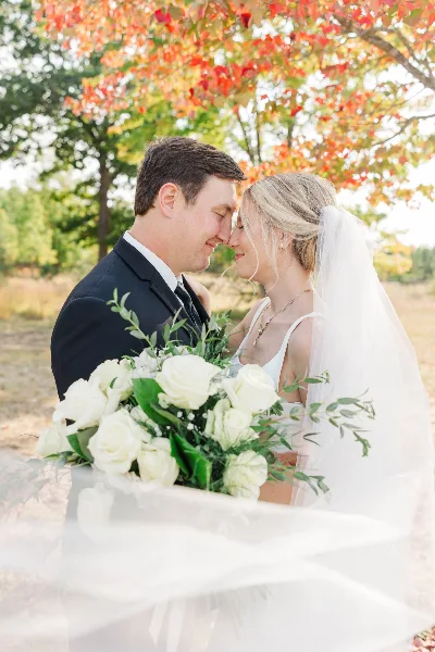 A bride and groom sharing a tender moment outdoors with a bouquet of white roses.