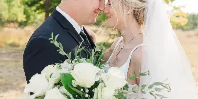 A bride and groom sharing a tender moment outdoors with a bouquet of white roses.