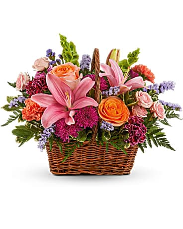A floral arrangement featuring pink lilies, orange roses, and purple flowers in a wicker basket.