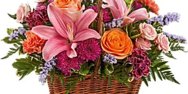 A floral arrangement featuring pink lilies, orange roses, and purple flowers in a wicker basket.