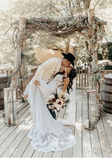 A bride and groom kissing under a rustic wooden archway on a wooden deck.