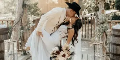 A bride and groom kissing under a rustic wooden archway on a wooden deck.